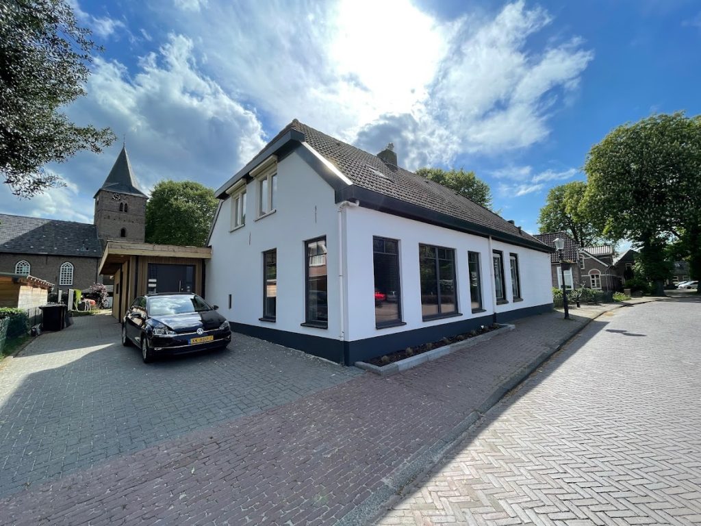 Woning met witte gestucte gevel en antraciet plint in een dorpsstraat