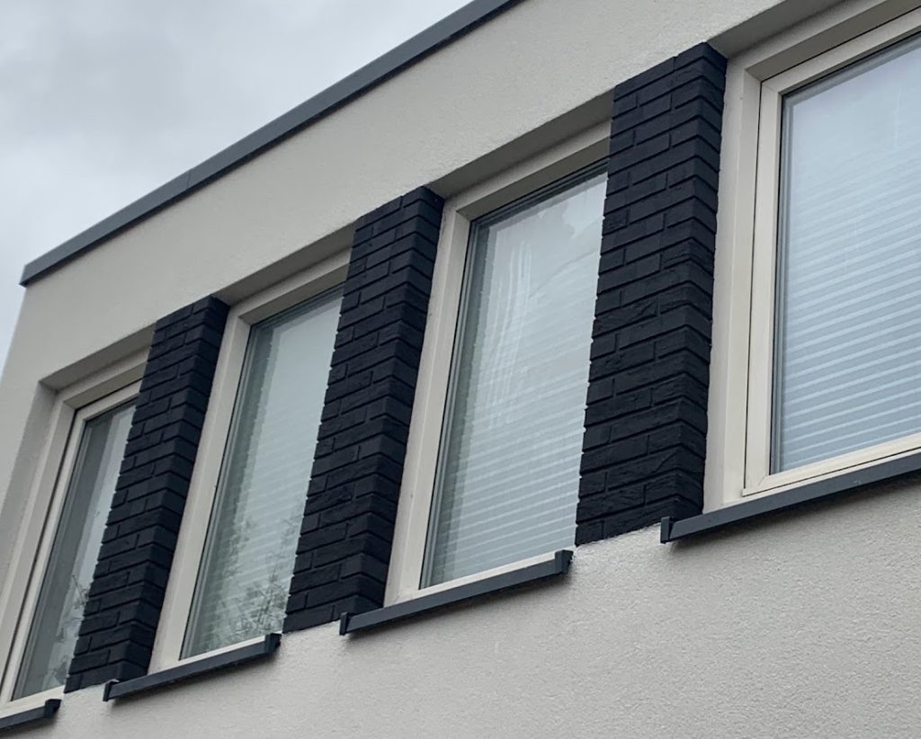 Detail van een gevel met sierpleister en donkere steenstrips rond de ramen