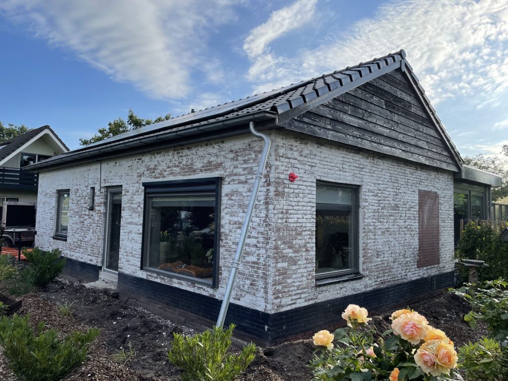 Witte woning met donker dak, zonnepanelen en tuin met bloeiende rozen